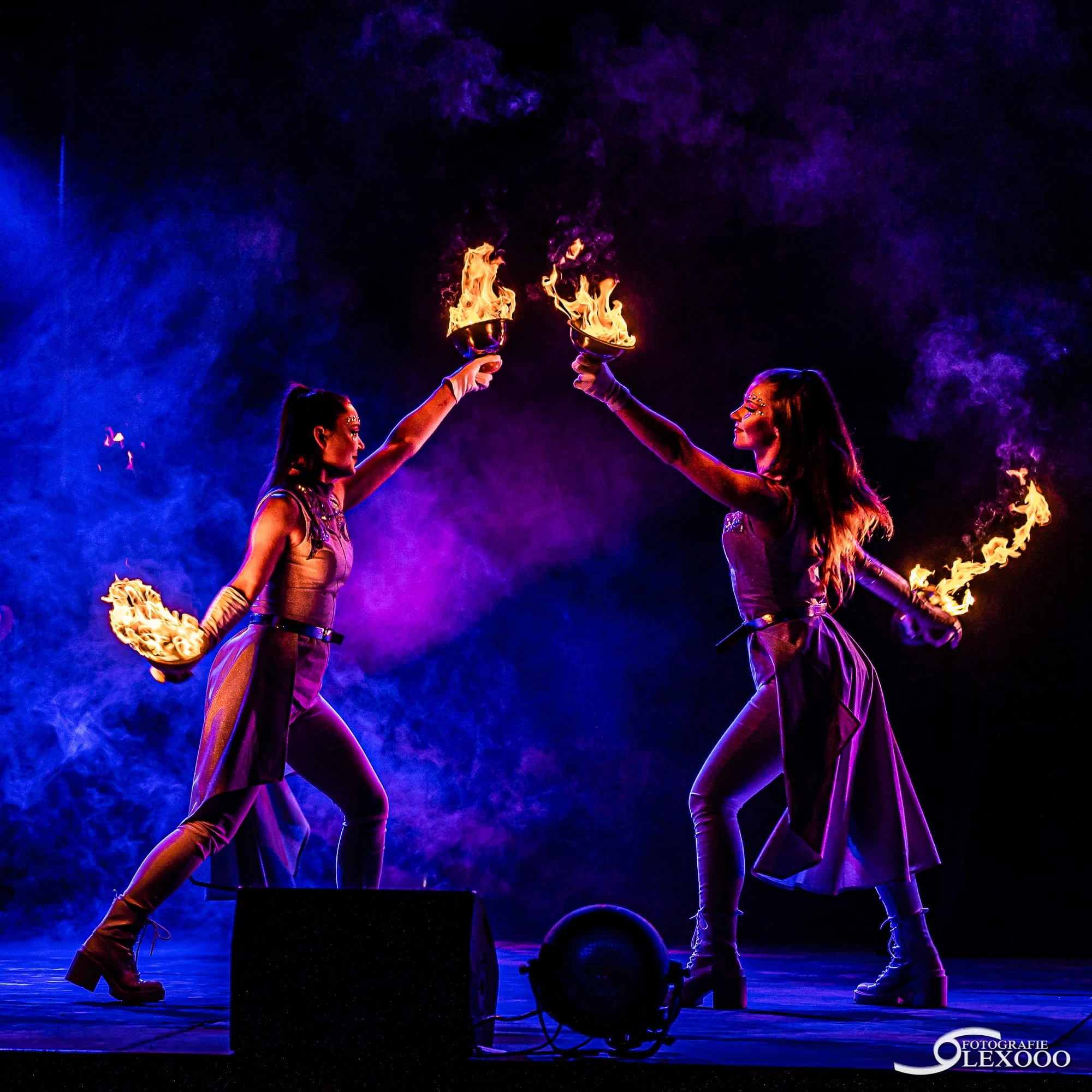 Twee vuurperformers met brandende schalen op een verlicht podium